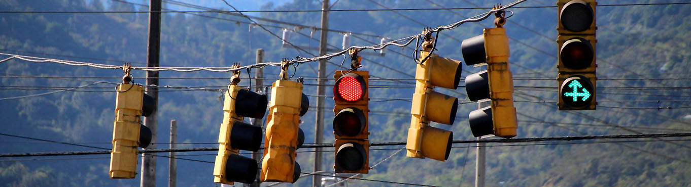 Several traffic lights hang from wires over a street in a mountainous area.
