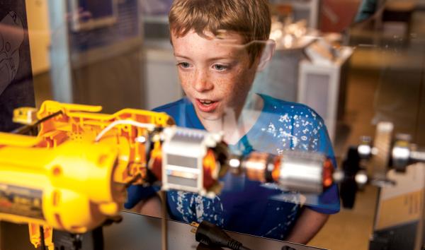 Another young boy is surprised and intrigued by the inner workings of an electric drill in the exhibit Amazing Machine.