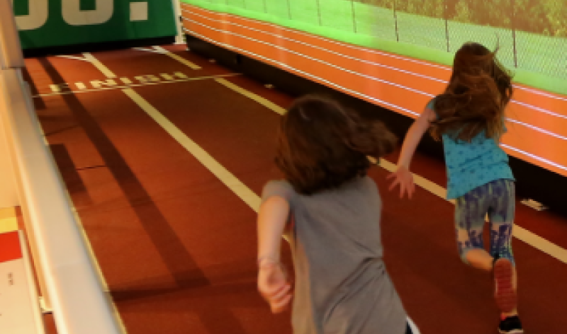 Two children run on the race track in the Sports Zone exhibit at The Franklin Institute.