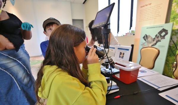 A girl looks into the eyepiece of a scientific instrument