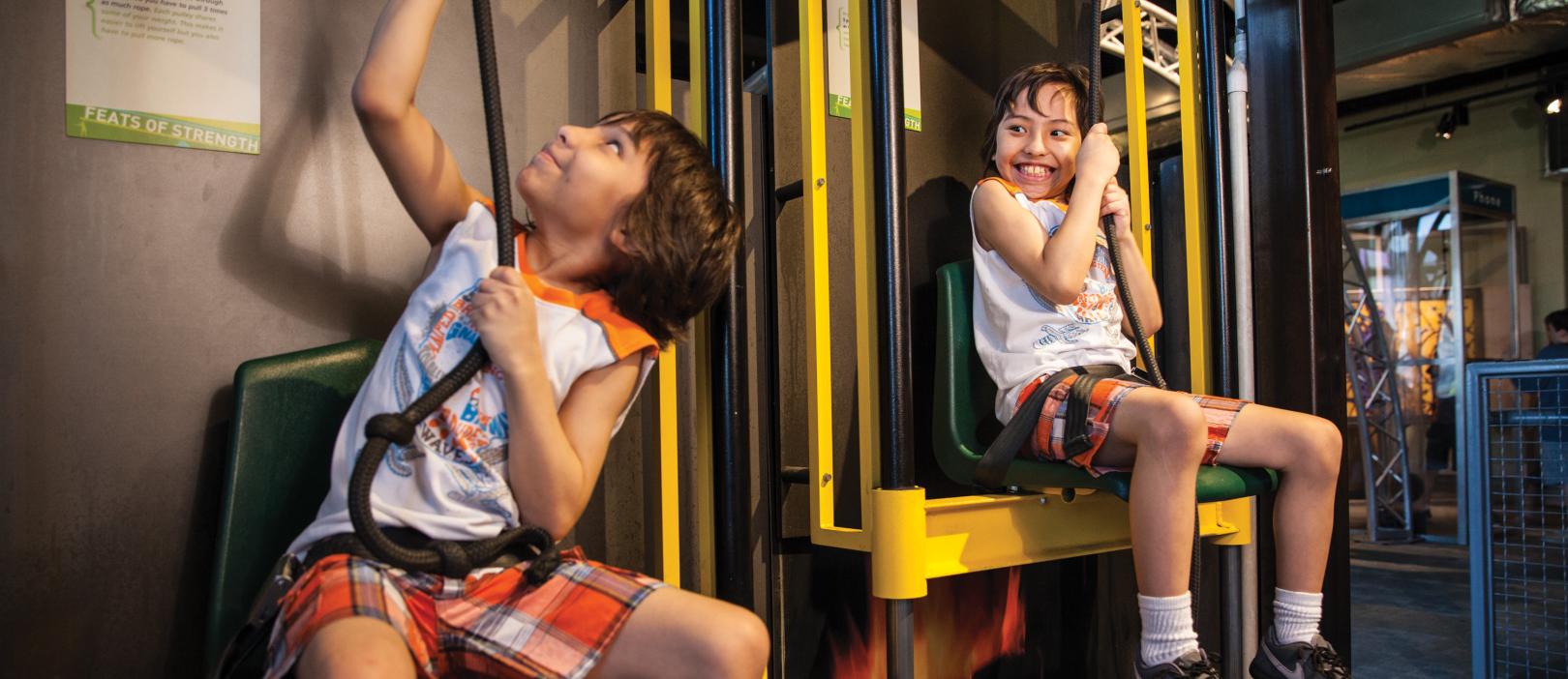 Twin boys learning and having fun lifting themselves on an interactive in Sir Issac's Loft