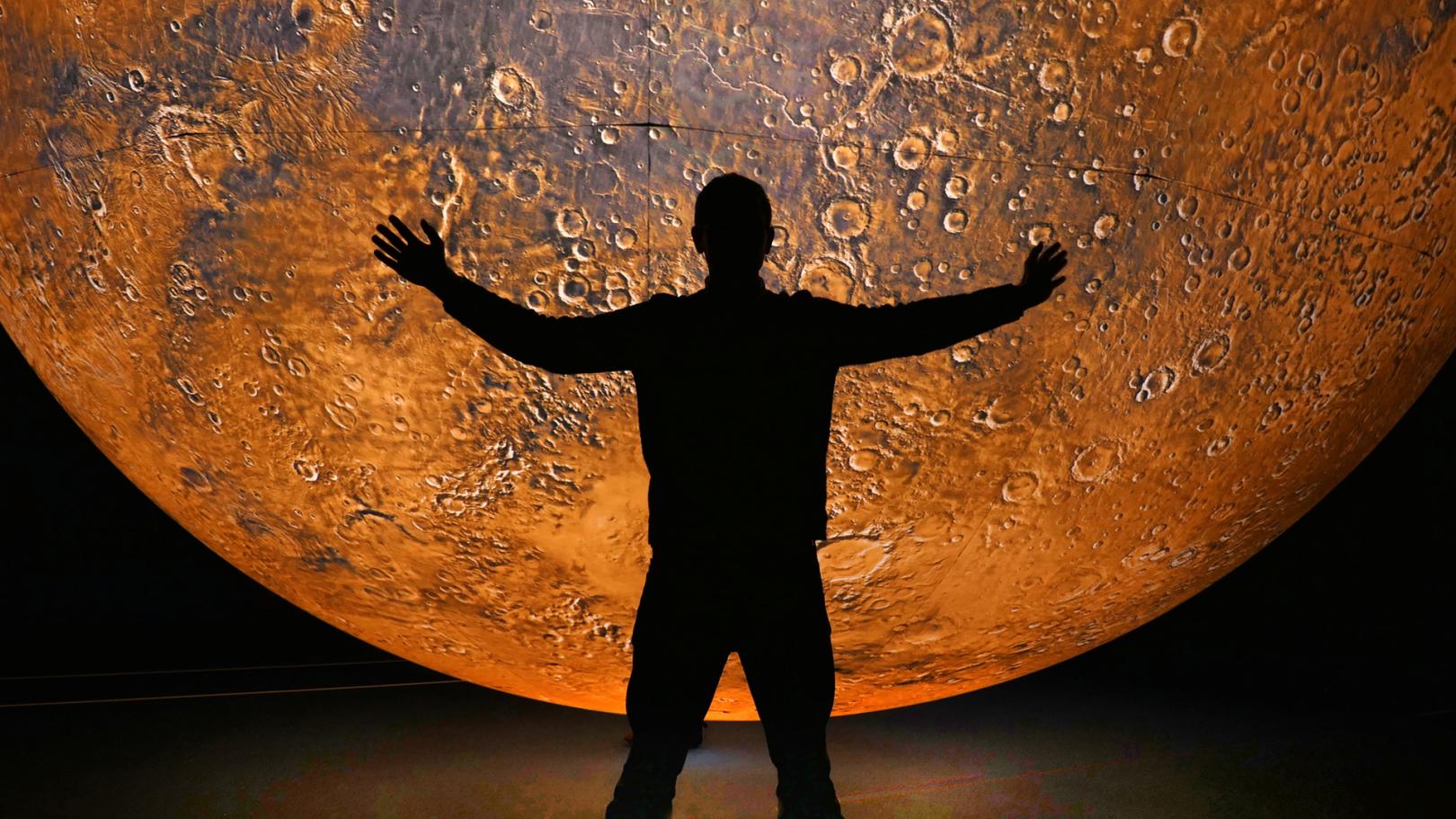 A person is outlined in black against "Mars," by artist Luke Jerram